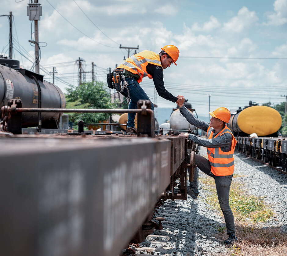 A worker helping another worker get on a rail train
